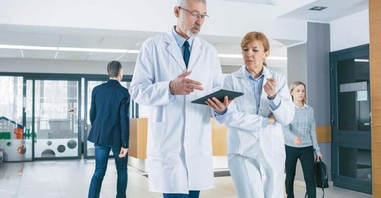 Doctor speaking to another doctor, while referencing a tablet with healthcare time and attendance software