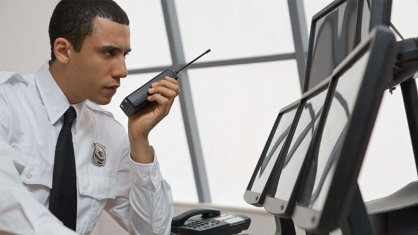 A university campus security officer reviewing a security tape and speaking over a handheld transceiver 1