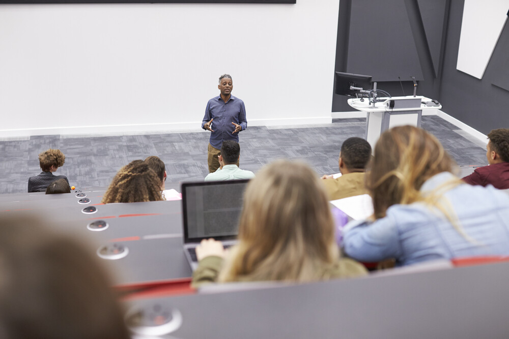 A professor lectures in front of a classroom, to portray a staff member benefitting from education time tracking
