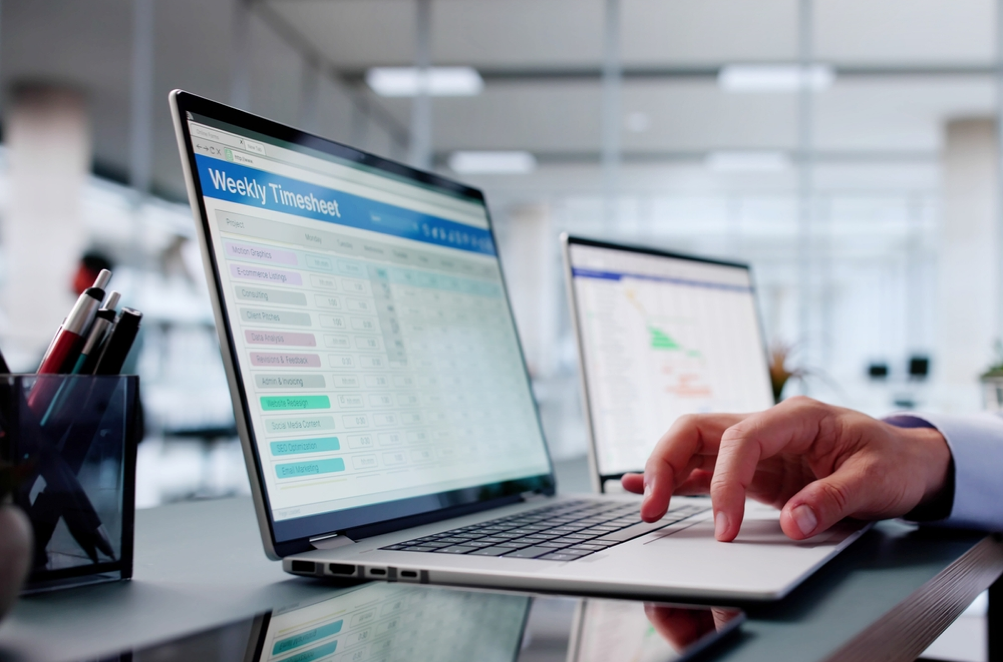 Visual representation of online timesheets in a laptop screen with someone scrolling through them with their hand on the trackpad