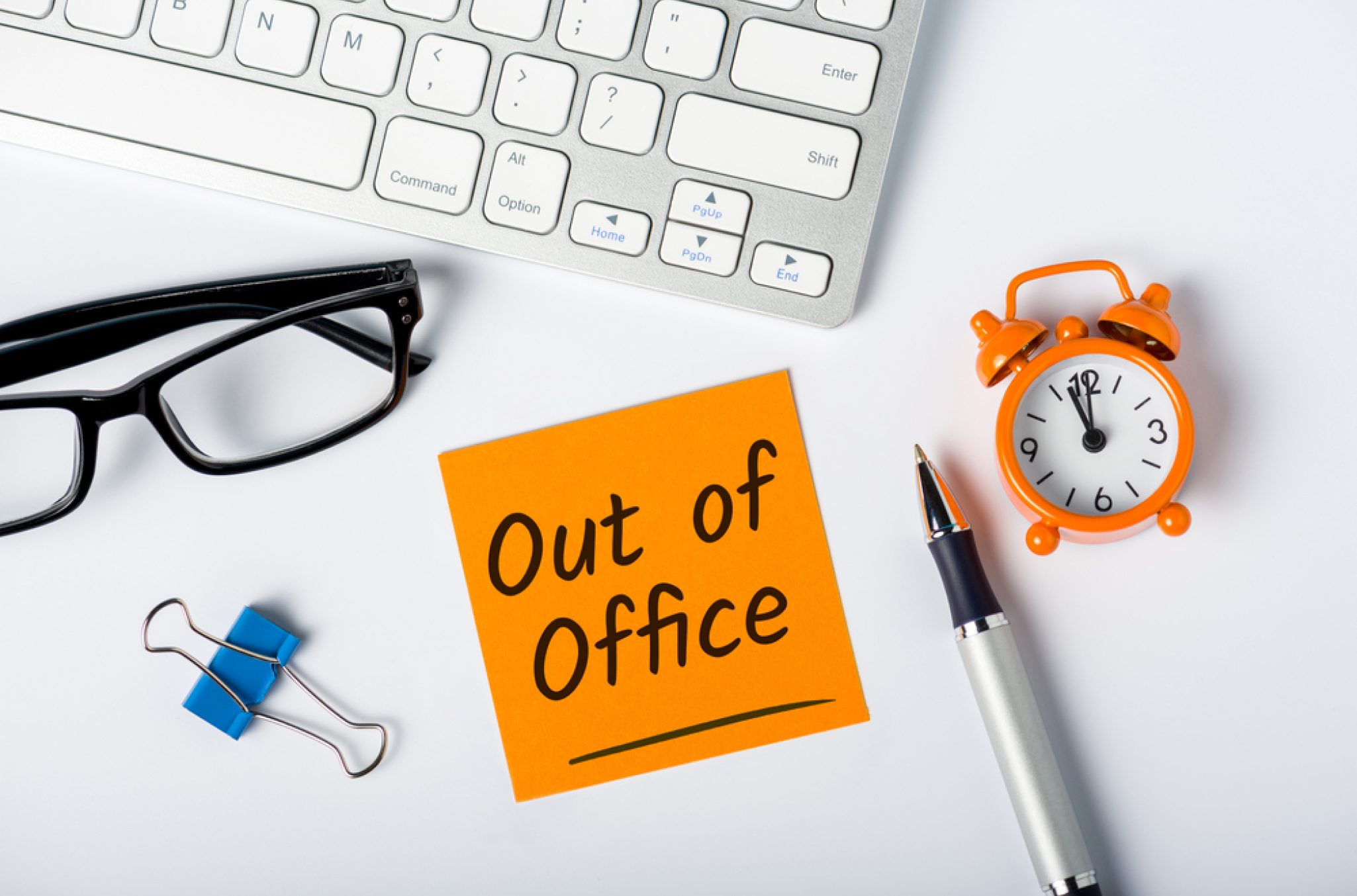 Visual representation of how pto works with an "out of office" sticky note on a flat white computer desk surface