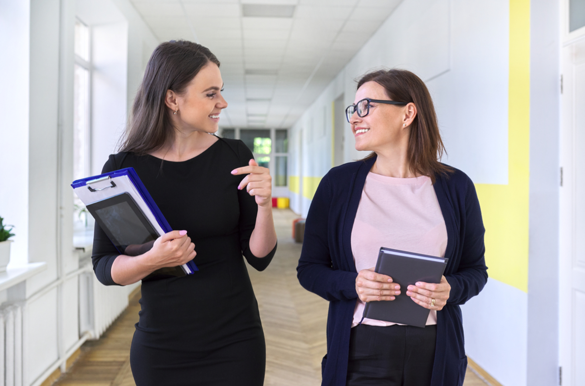 Two female employees walking side by side, exchanging conversation as they go, about HR policies and how to keep track of employee leave