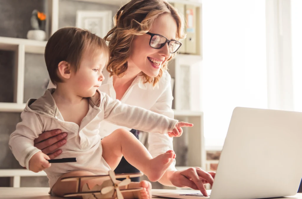 A mom at home with her child, checking in on her laptop which demonstrates the success of her leave of absence