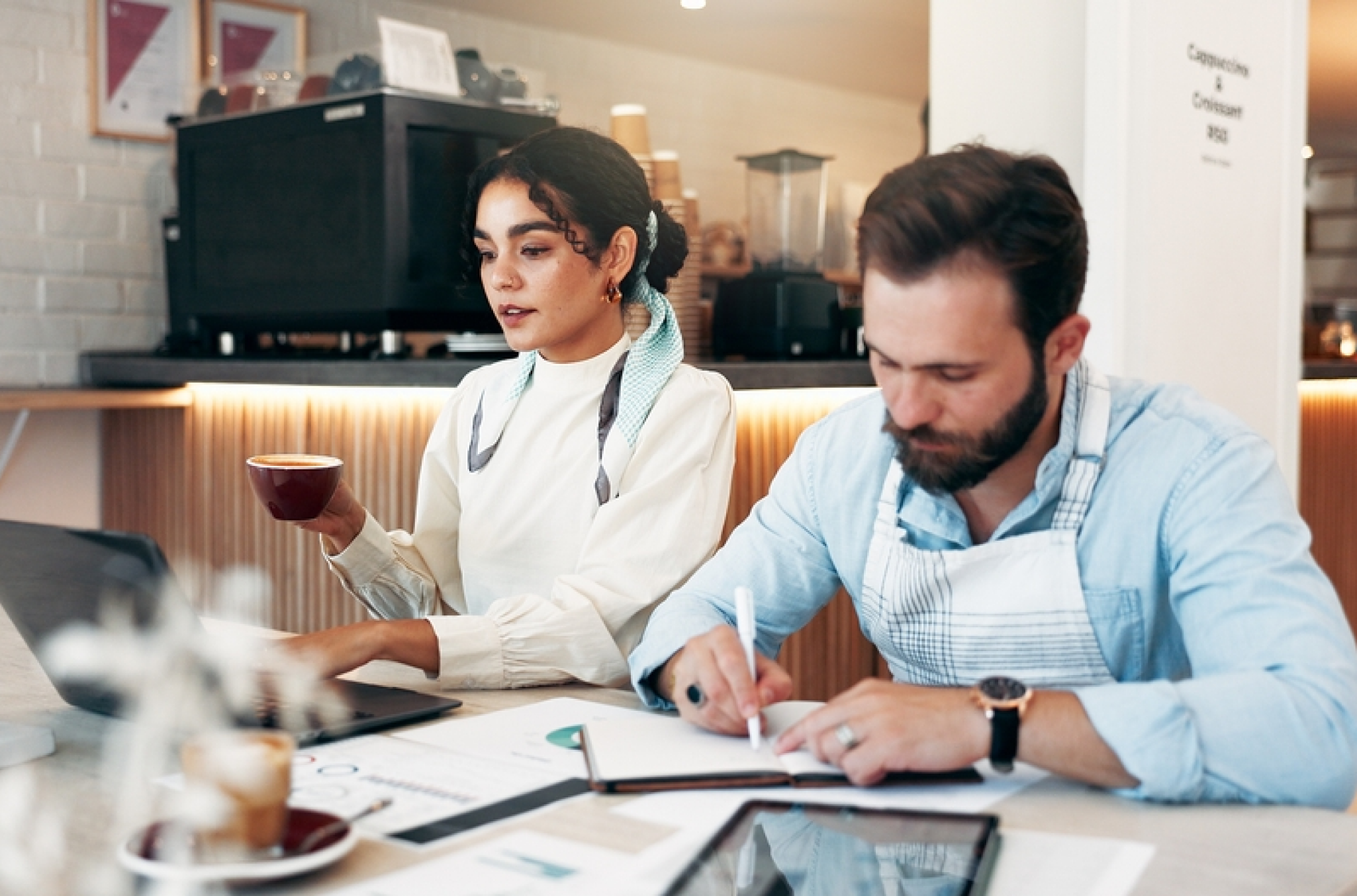 A man and woman reviewing how they're going to approach employee scheduling in hospitality, in a small coffee shop space