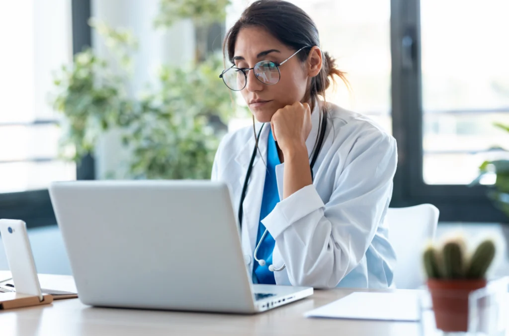 Doctor looking at her laptop trying to track time manually in frustration, showing a representation of why the organization needs employee time tracking software, as