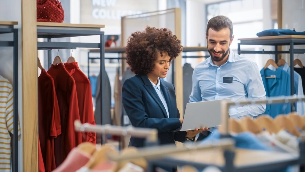 Two retail employees looking at their scheduling software on a tablet and discussing labor forecasting for the month ahead