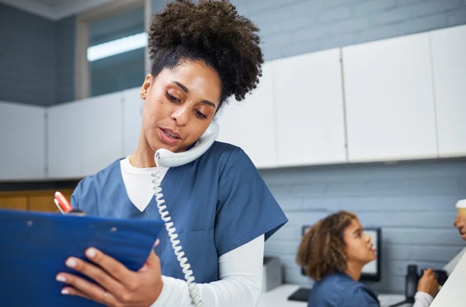 Practice administrator standing with a phone on her shoulder, going through a checklist of healthcare time and attendance challenges to solve for in the coming weeks as they implement a new system