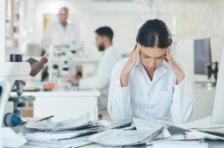 A frustrated female lab radiologist looking down at a stack of payroll paperwork, illustrating some of the hidden costs of poor time management in healthcare