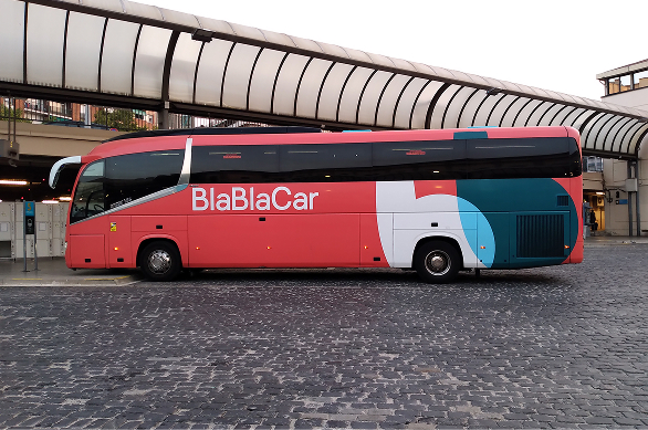 reddish orange long bus with "BlaBlaCar" logo on it parked outside a bus station
