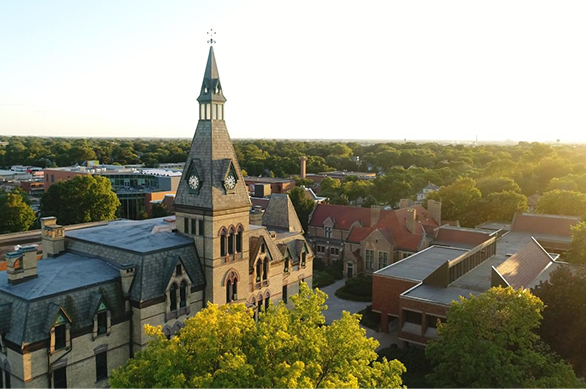 Gothic-looking chapel and steeple and building against shorter bright green trees