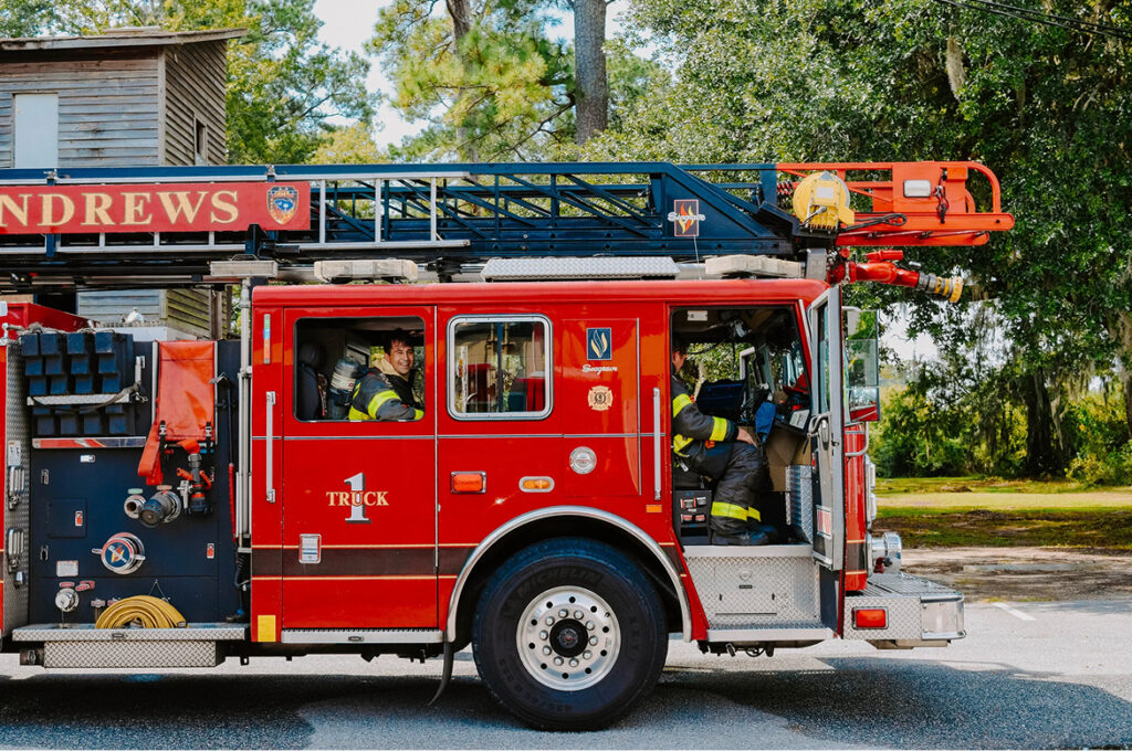 Horizontal view of front end of bright red fire truck with tall trees in the background