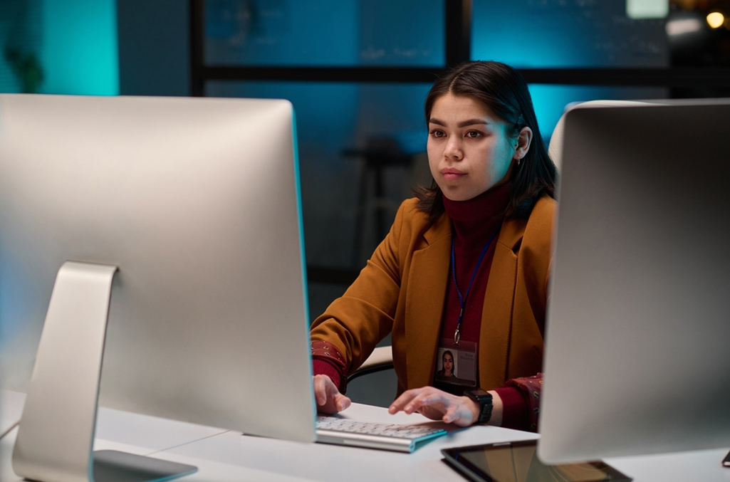 A female worker at her desk in front of a big computer monitor, managing the government time and attendance software on screen