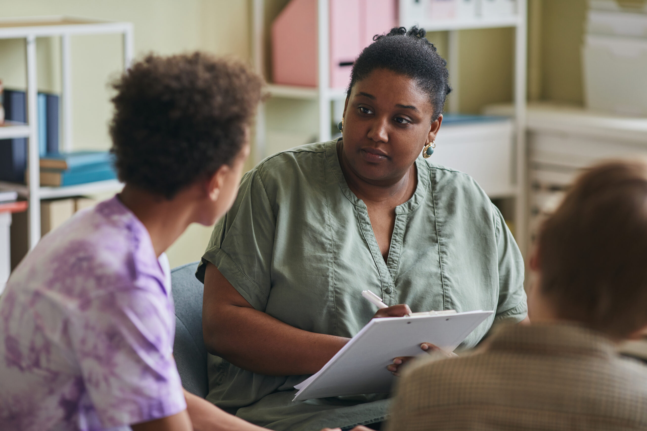 African American psychologist listening to teenage boy and making notes, she working with difficult teenagers at class