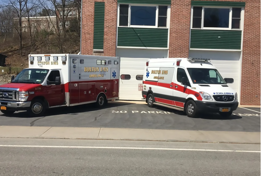 Two EMS vehicles parked with nose of vehicles pointed to the left and right hand corner to make a V shape and parked in front of a closed garage at an EMS station
