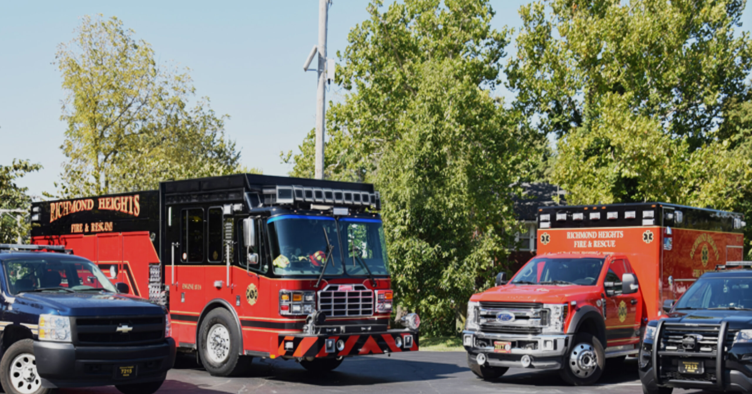 Two East Central Dispatch firetrucks pointed towards one another alongside the front half of two police vehicles in front of very tall green trees