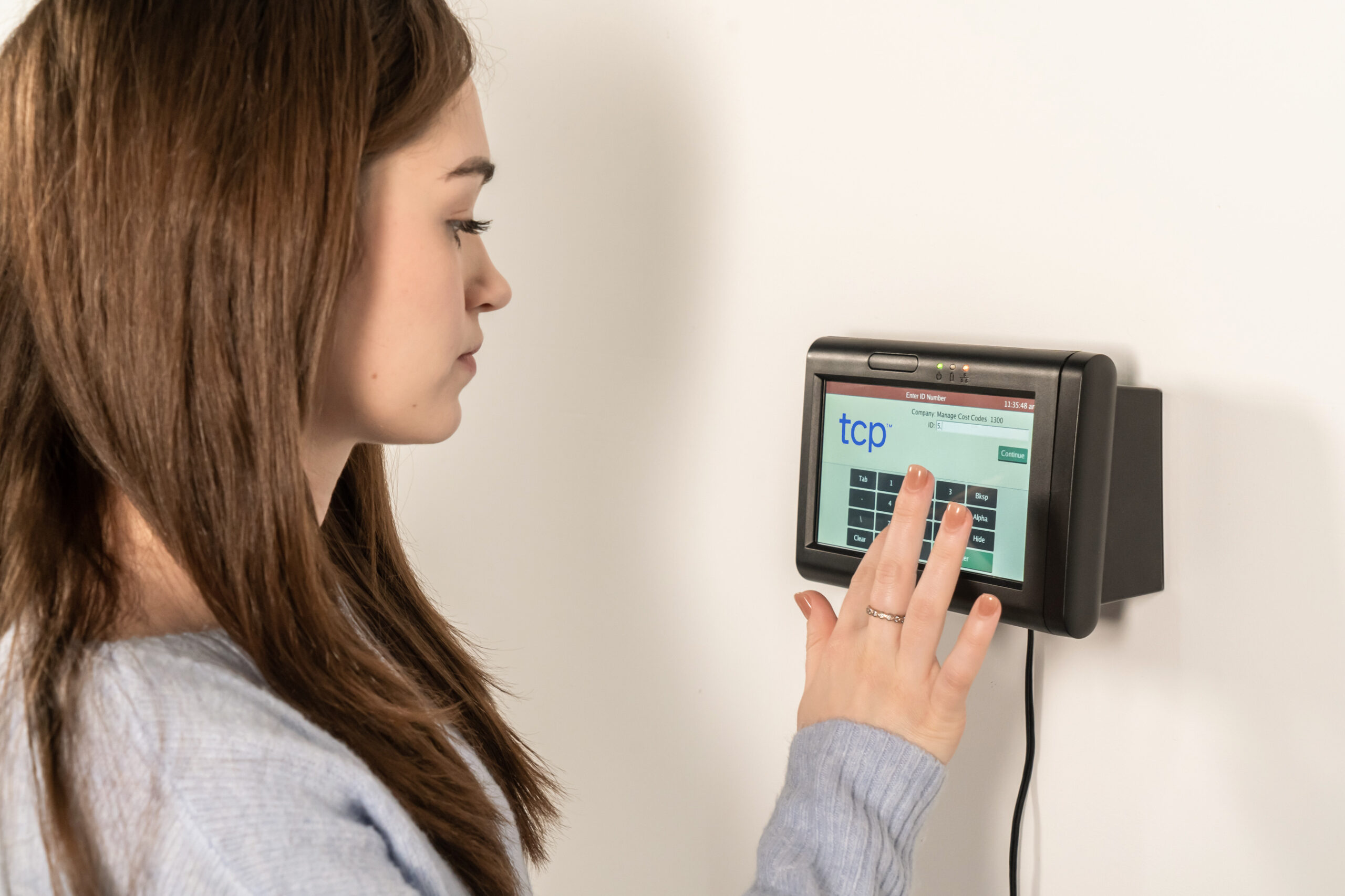 A woman using a keypad entry and badge scanner on a physical time clock