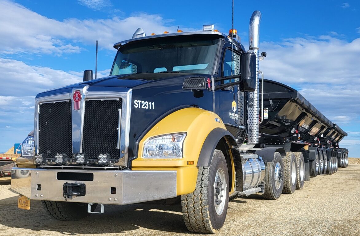 Front of black and yellow big rig truck on a sandy, gravel road